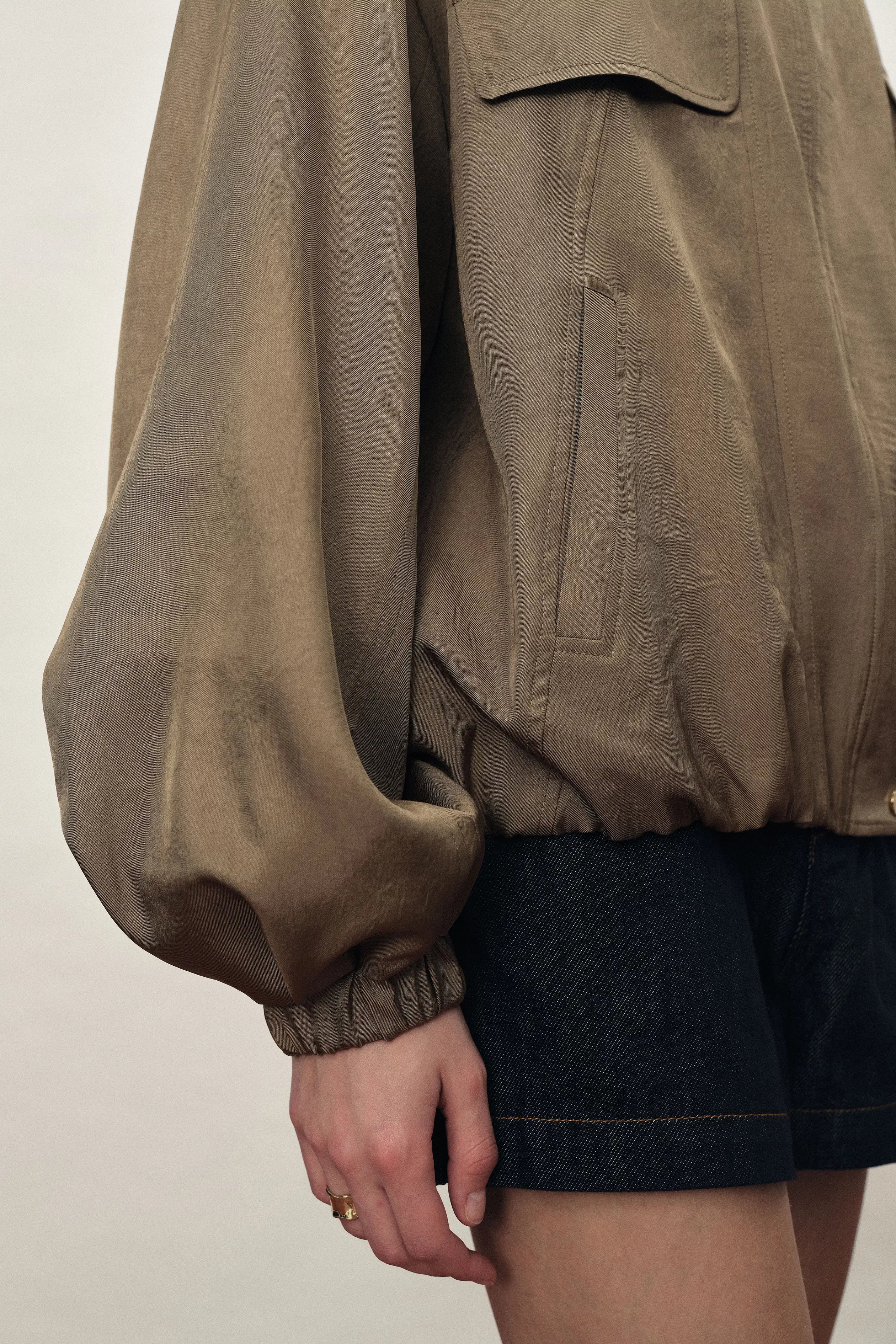 Brown satin acetate jacket with a bubble hem and utility pocket over dark denim shorts