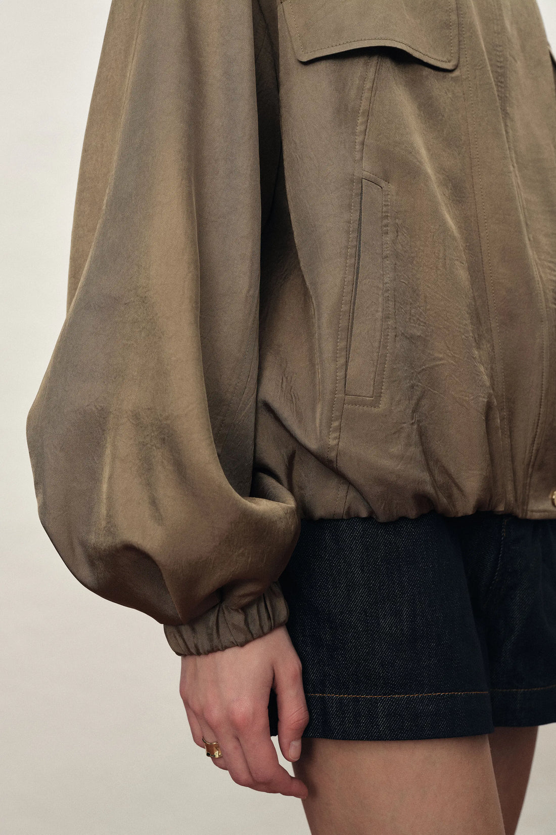 Brown satin acetate jacket with a bubble hem and utility pocket over dark denim shorts