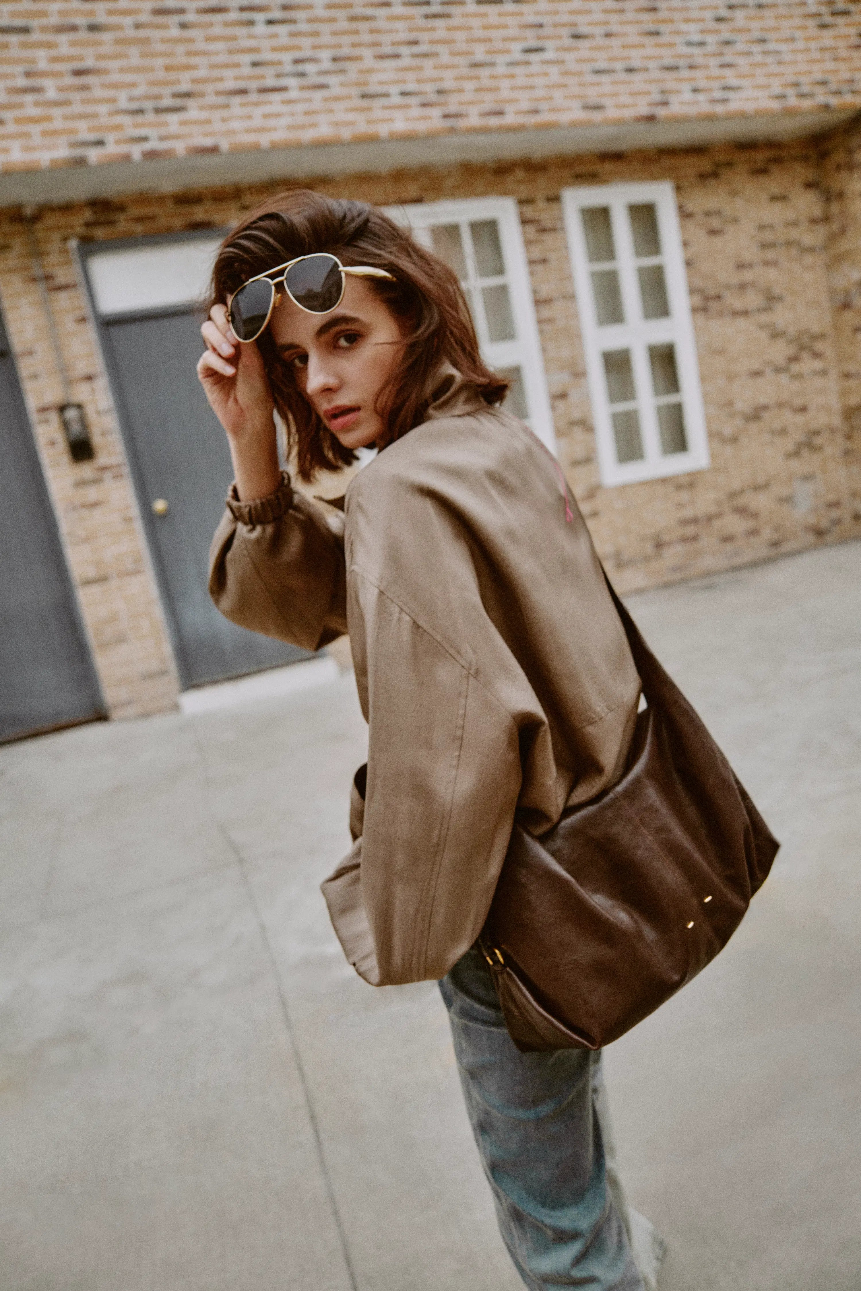 Woman wearing a taupe satin jacket with a shaped bubble hem and gold hardware outdoors